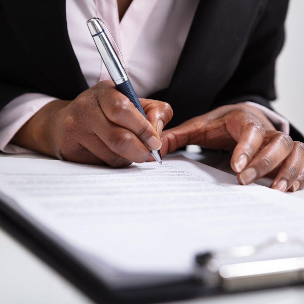 woman's Hand Signing On Papers Over Desk