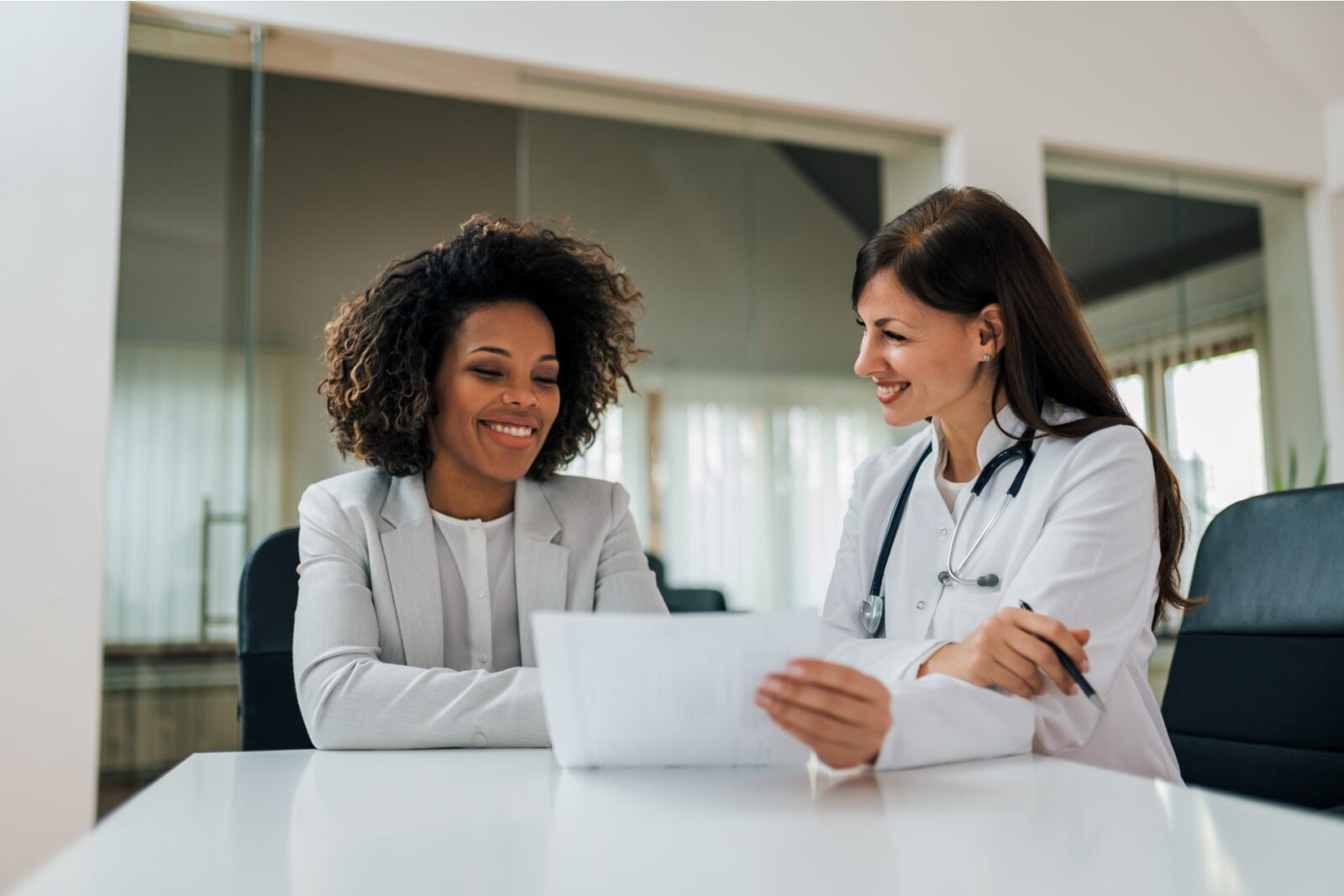 Smiling female patient and doctor looking at paper document.